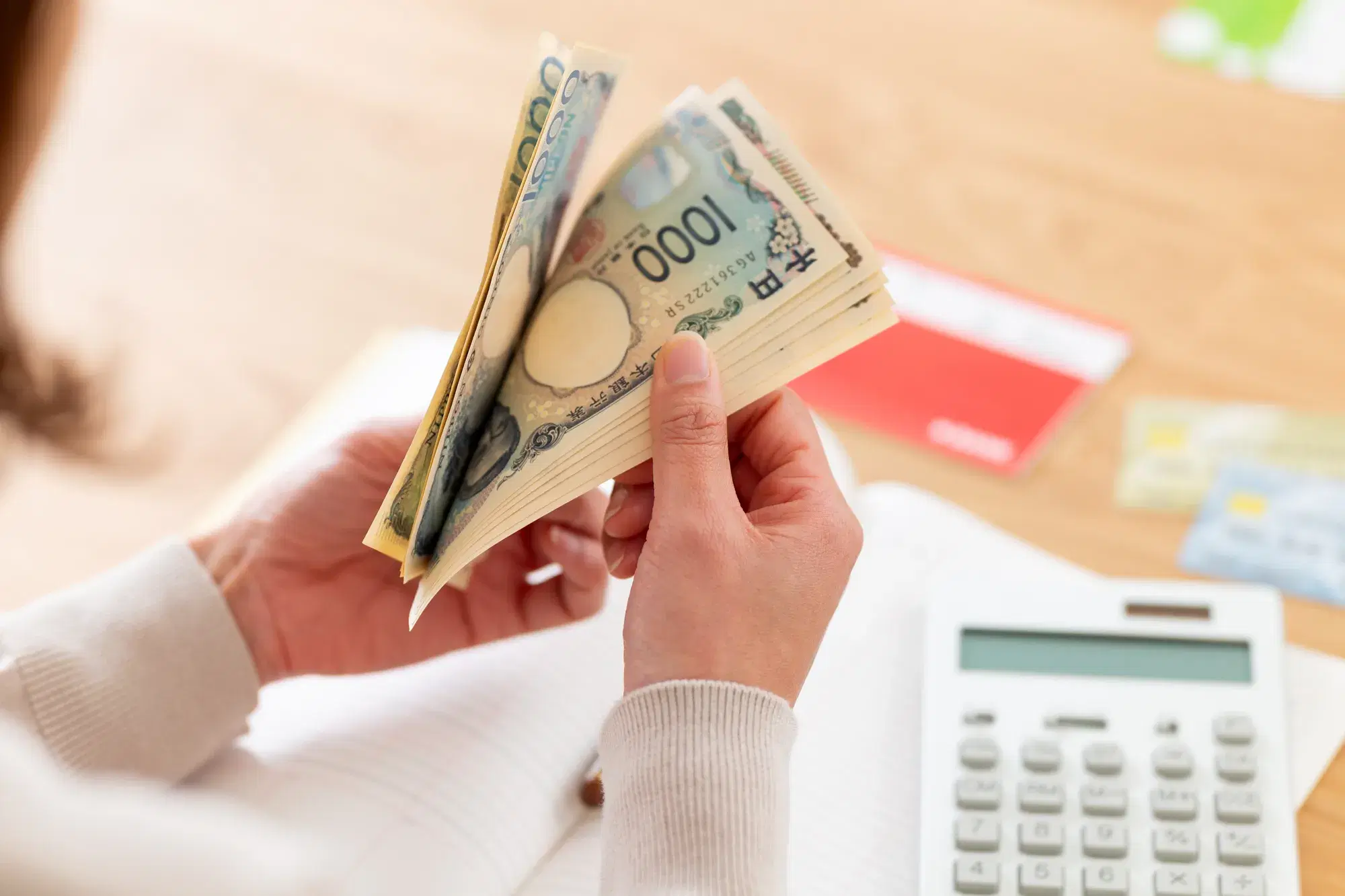 通帳と電卓と多数の千円札を数えている女性