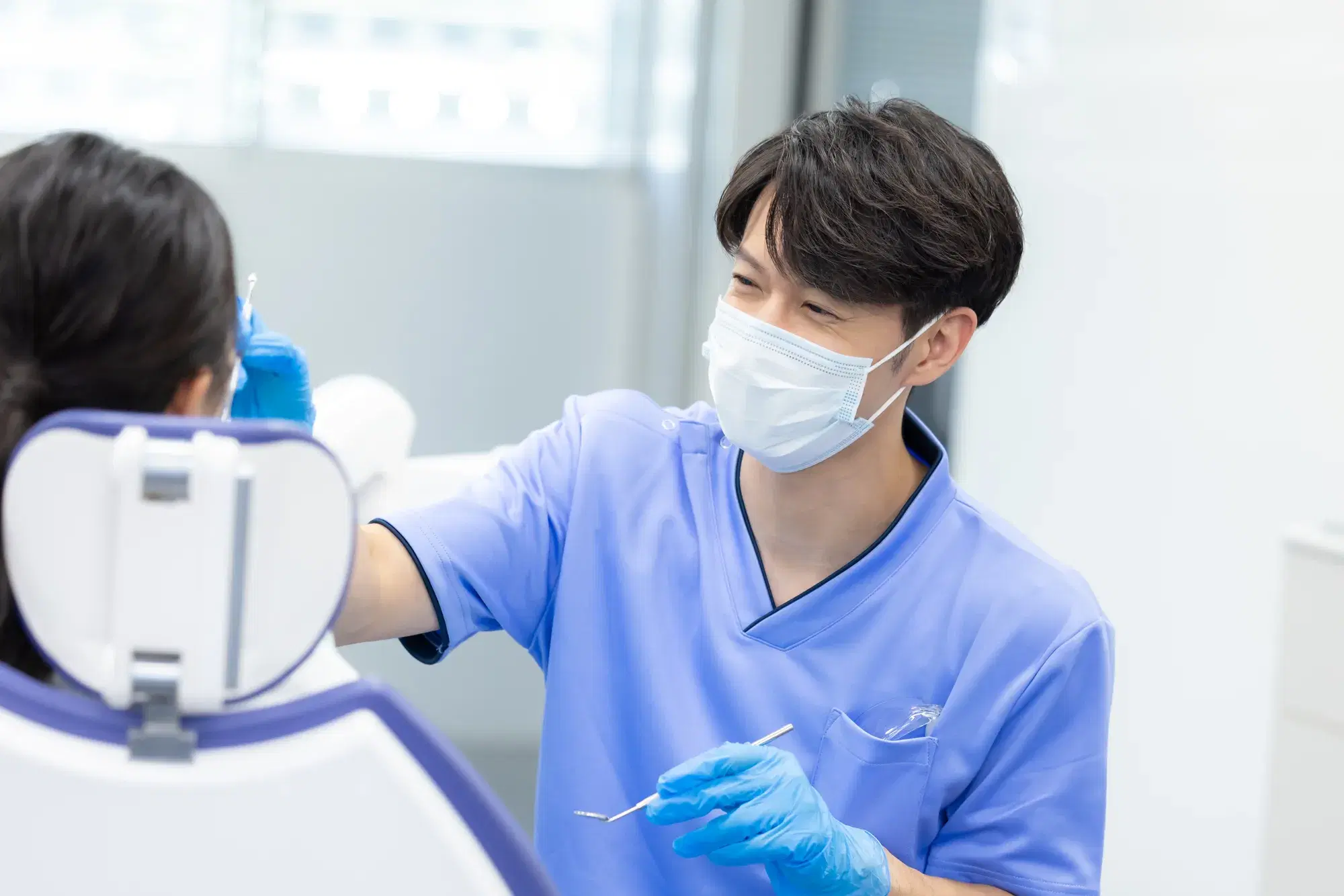 歯科医師が座っている患者を青いゴム手袋を着用して器具を用いて対応