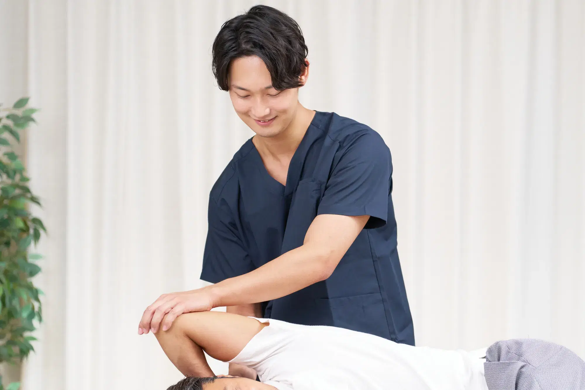 黒い服を着た整体師が白い服を着た男性の腕を処置している