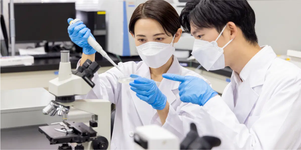 顕微鏡とピペットを使用する研究員の男女たち