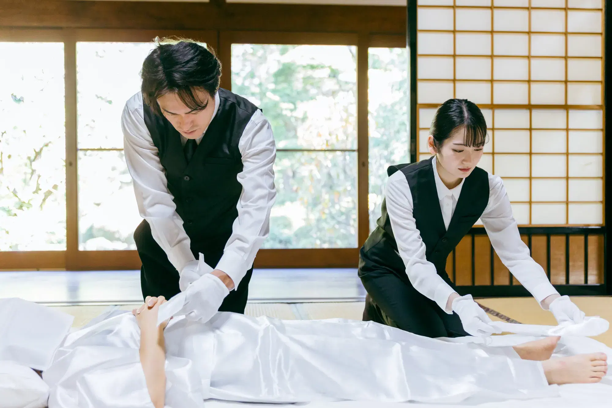 葬儀屋の男性と女性が遺体の処置をしている。