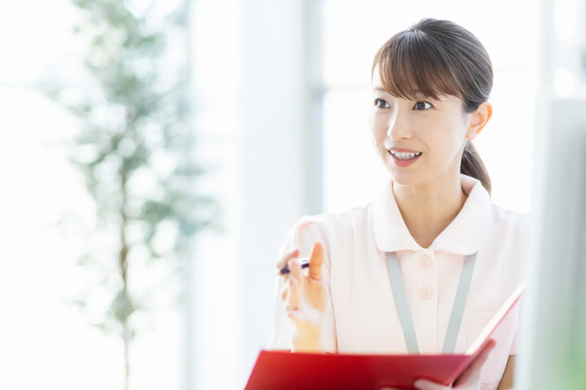赤色のバインダーを持ったピンク色の服を着た女性