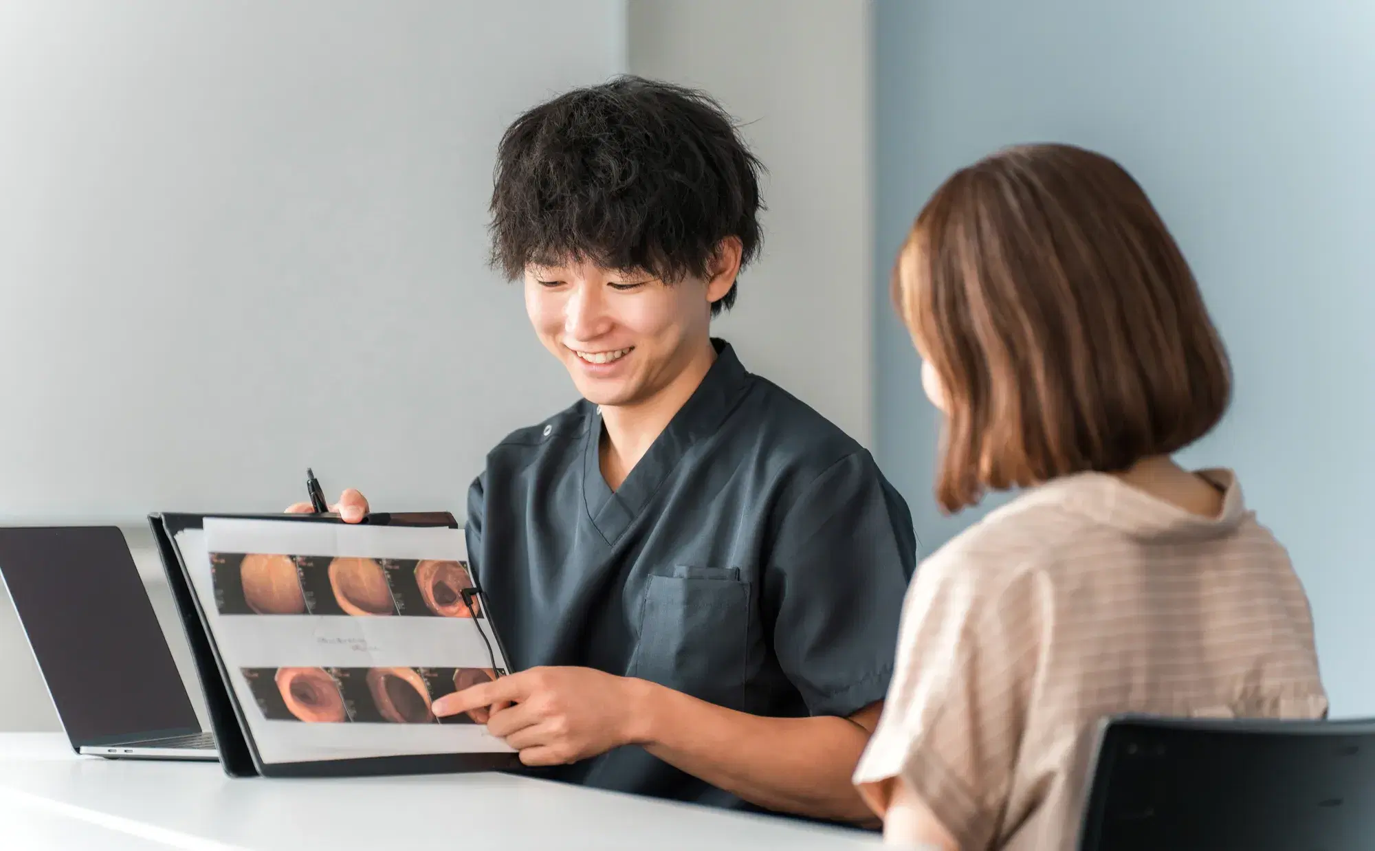 黒いスクラブを着た男性がベージュのボーダー模様の服を着た女性に説明をしている