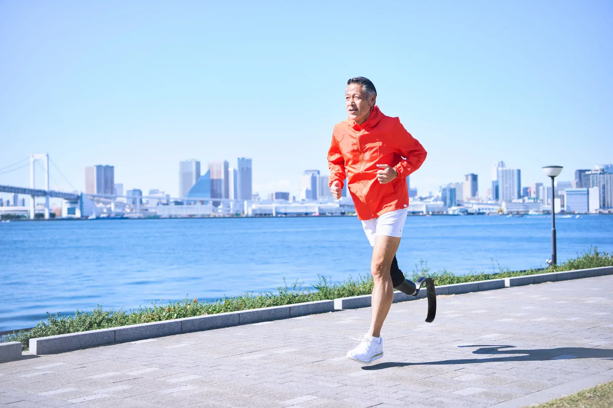 オレンジ色の服を着た男性が義足を付けた状態でランニング