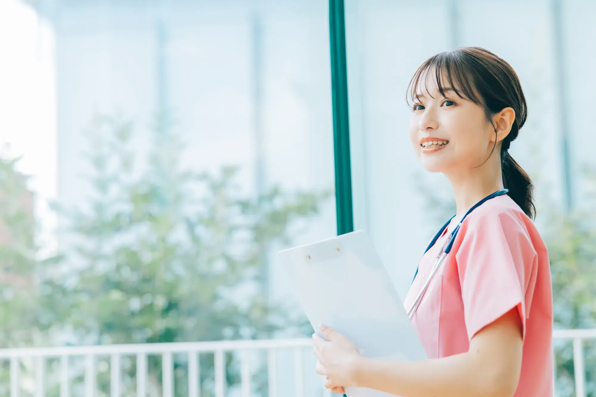 首から聴診器を下げたピンク色の服を着た女性