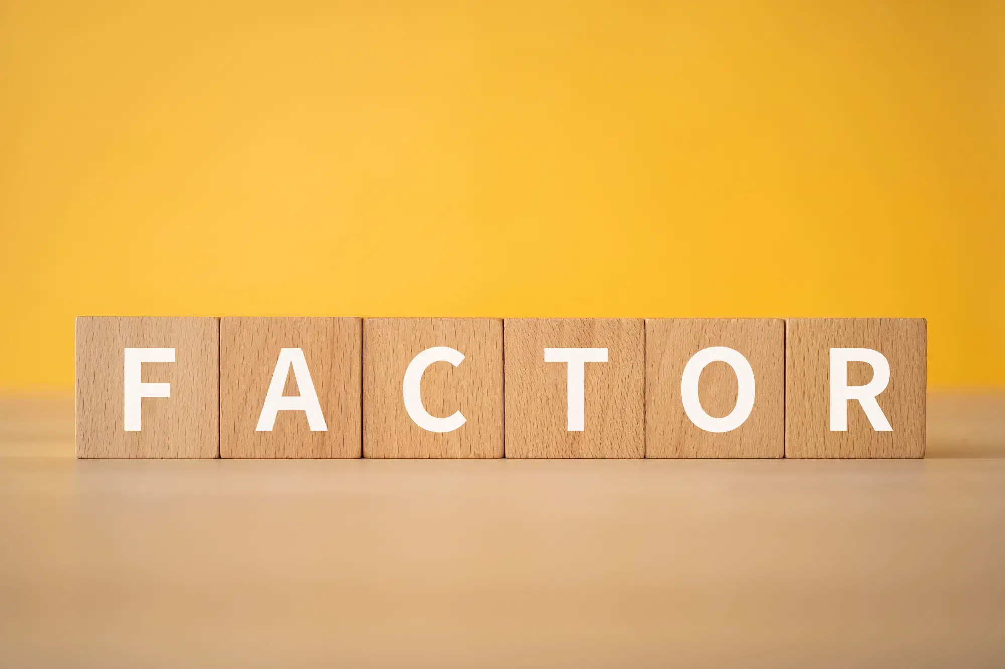 黄色い背景に木製の積み木が置いてあり、積み木にはfactorという白い文字が書かれている。