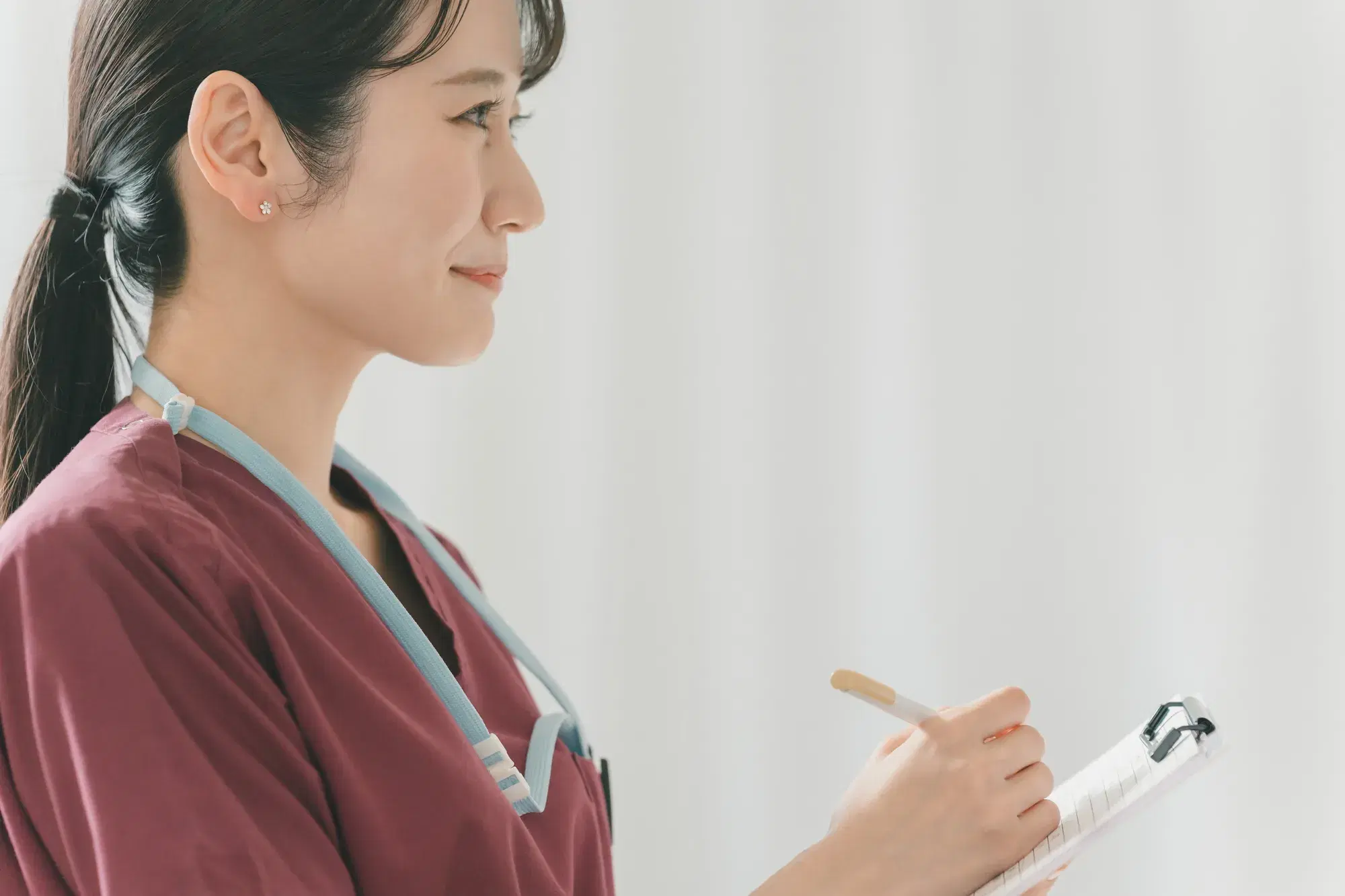 えんじ色のスクラブを着た女性が笑顔を浮かべながらメモを取っている。