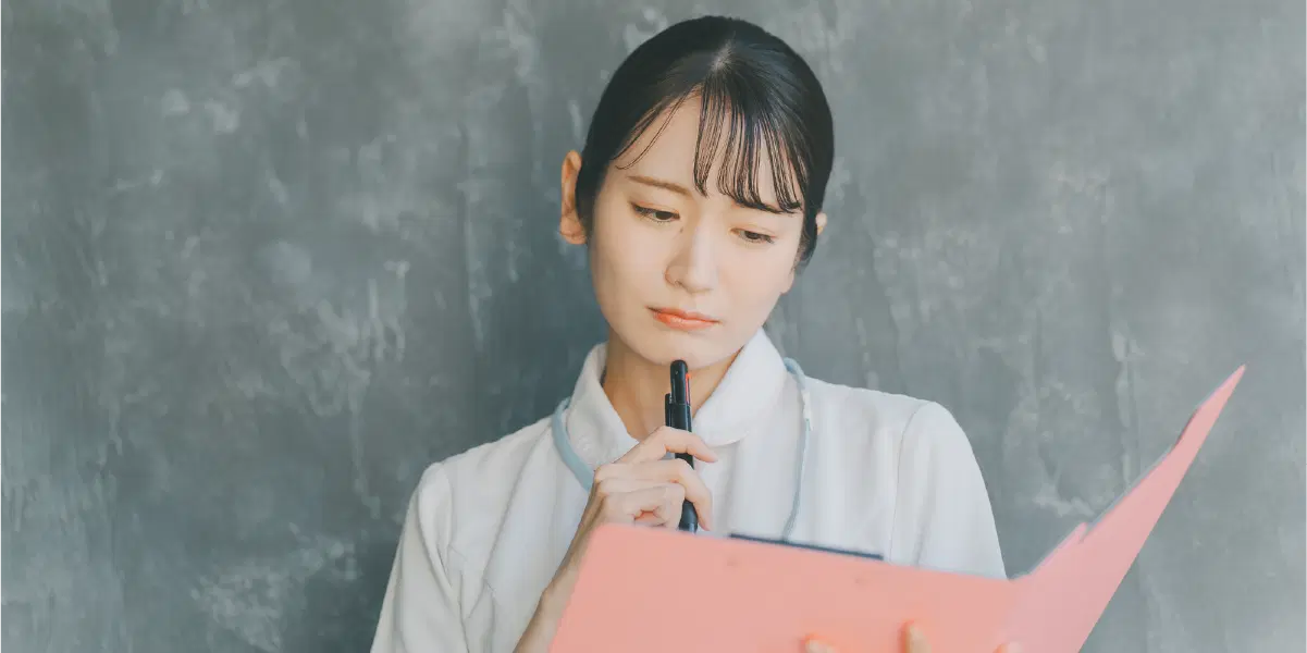 ピンクのバインダーを持ち顎にペンを当てている女性