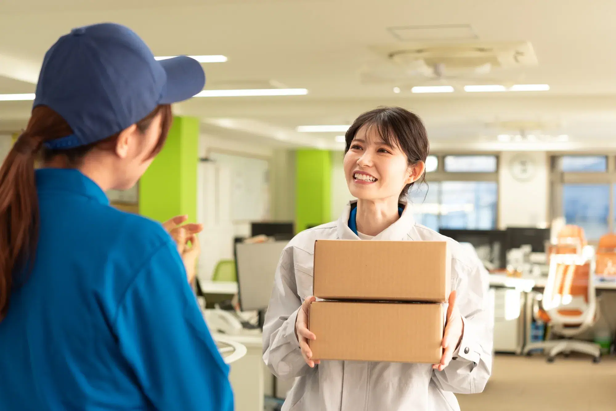 青い服を着た配達員がオフィスに配送物を女性に届けている