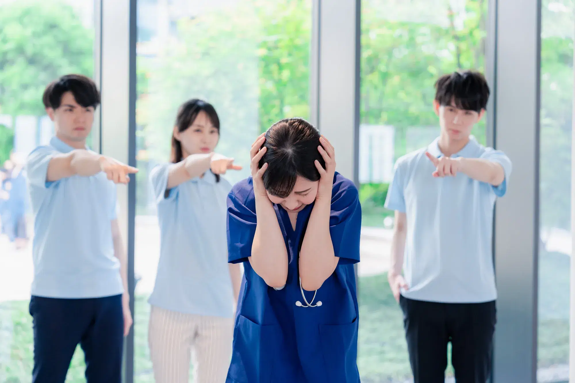 水色の服を着た人たち全員から指をさされている聴診器を首から下げている青い服を着た女性