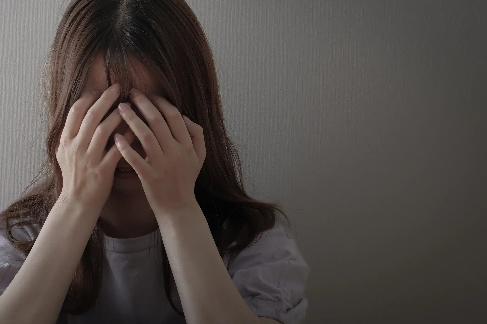 暗い空間で白い色の服を着た女性が顔を両手で覆う