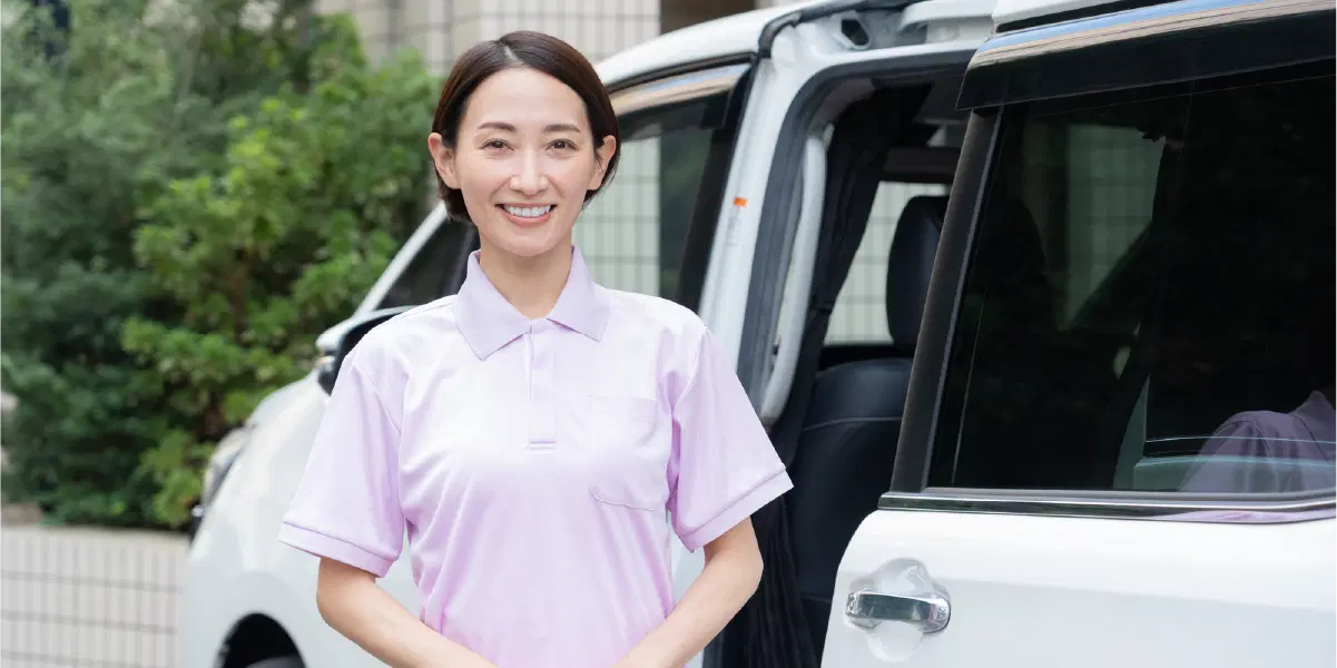 車を背景に笑うピンクの服を着た女性