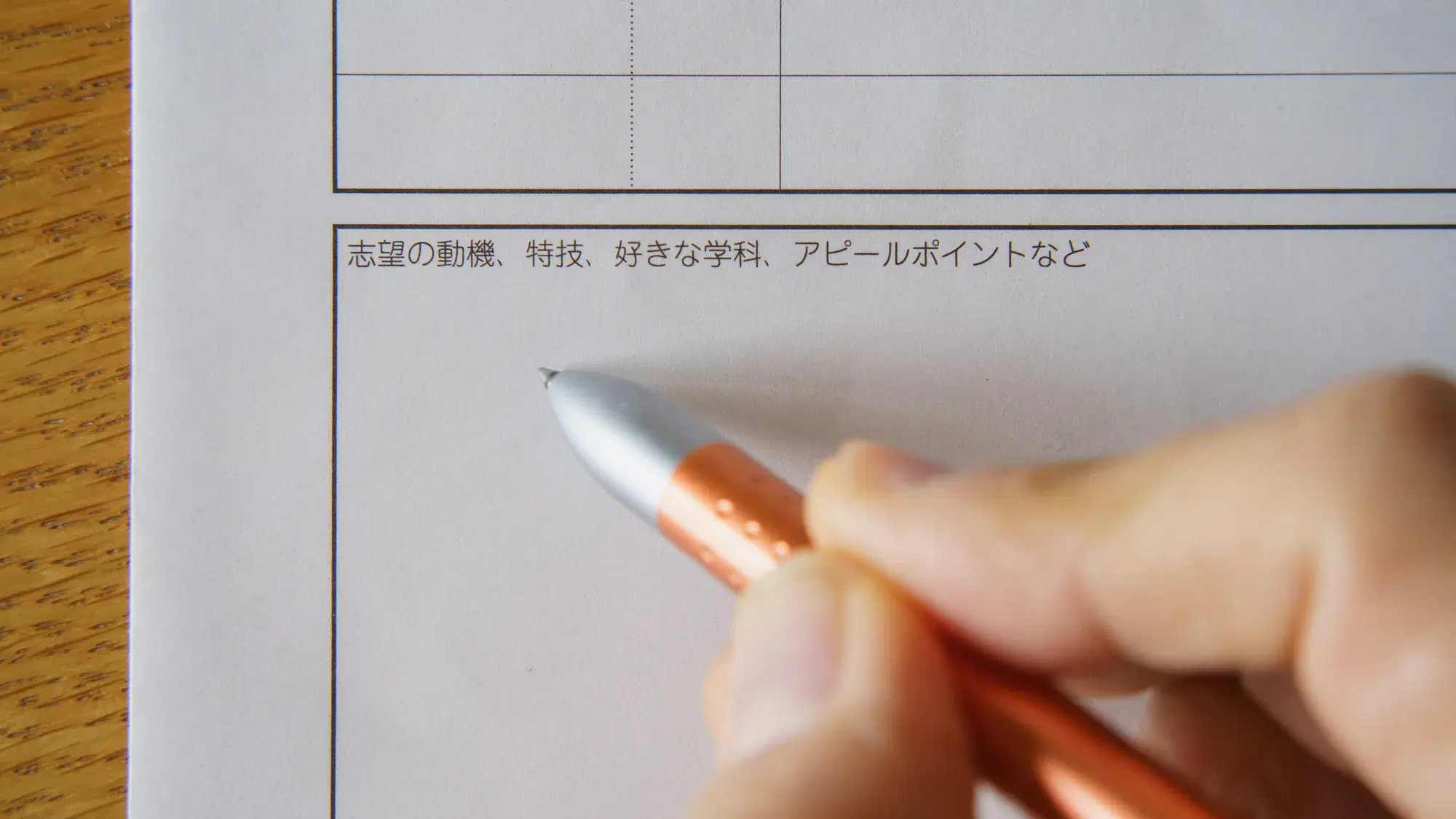 履歴書にペン先が銀色のオレンジ色のペンで記入をしようとしている。