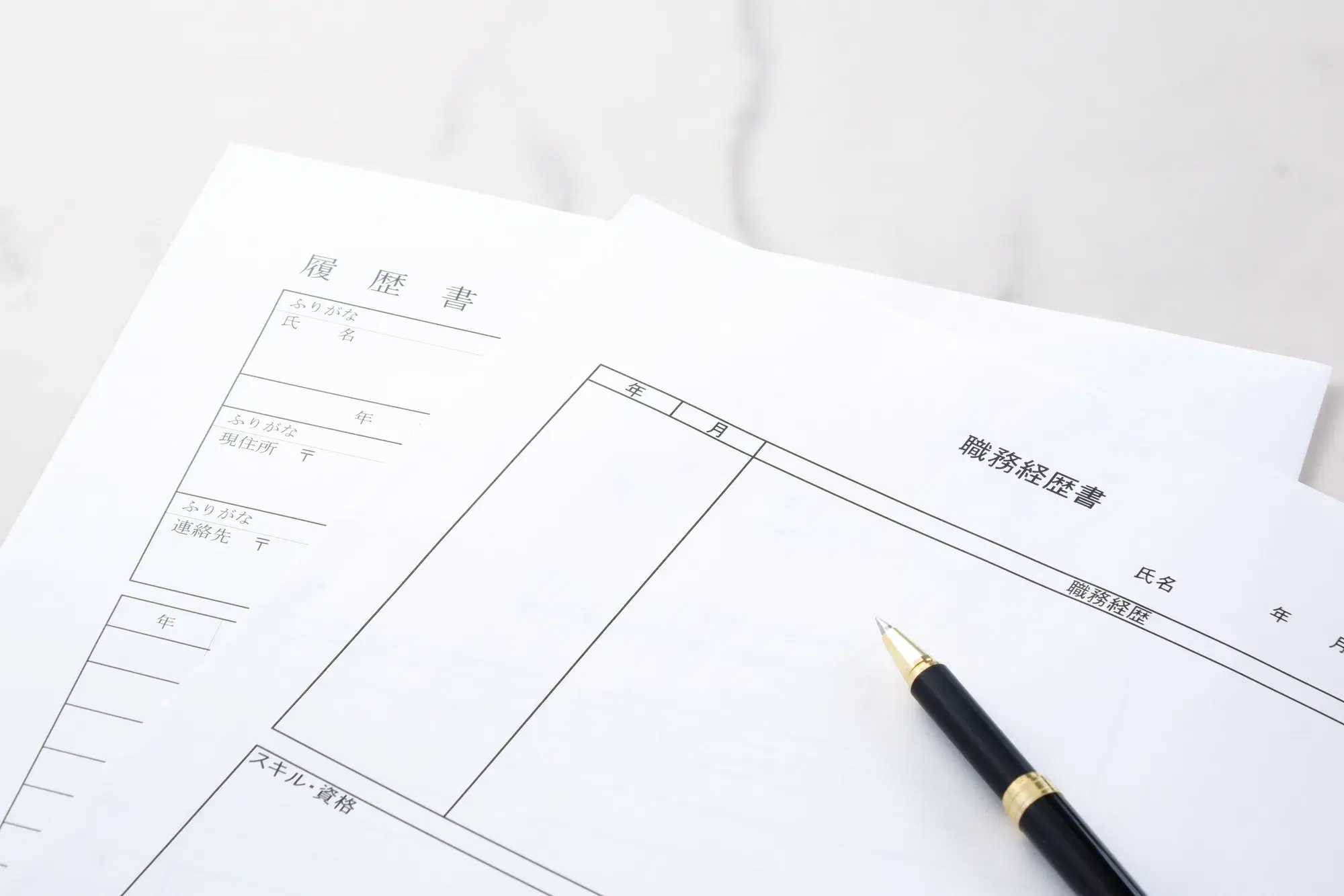 「履歴書」と「職務経歴書」と書かれた用紙の上に、黒色のペンが置かれている様子が写っている。