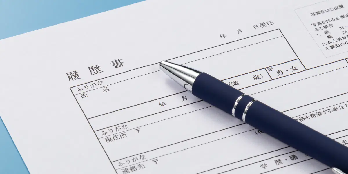 水色の背景に履歴書と黒いボールペンが置いてある