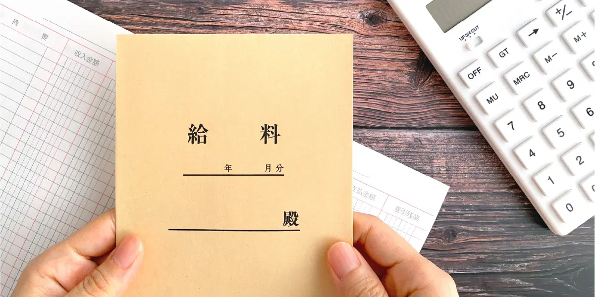 給料袋を持つ手と机の上に計算機がある