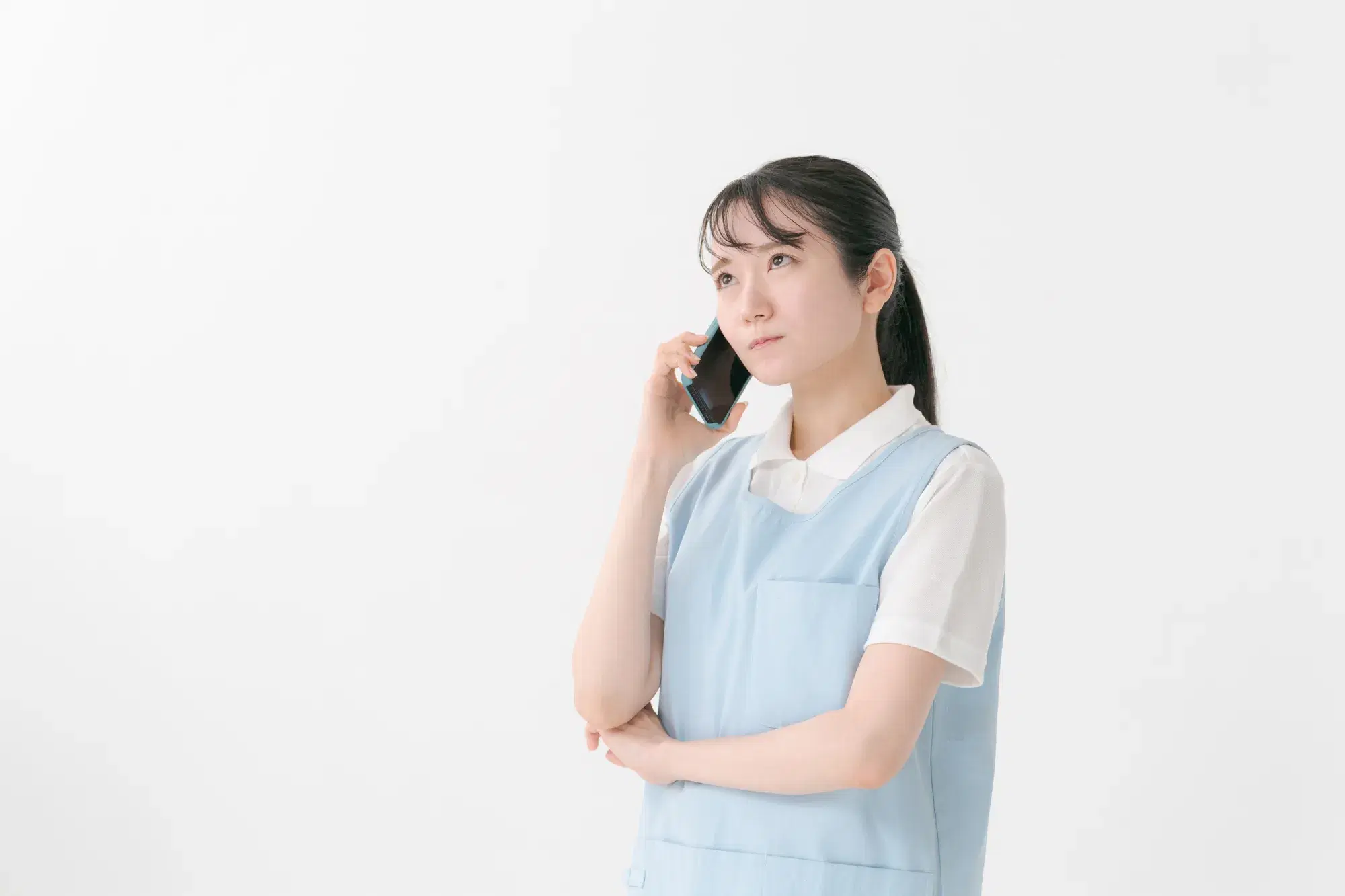 水色のエプロンを着た女性が右手にスマホを持ち右耳に当てがって電話
