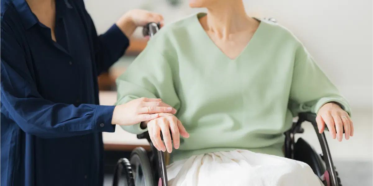 左手をブレーキにかけたまま右手で腕を触る人と車椅子に座っている高齢者