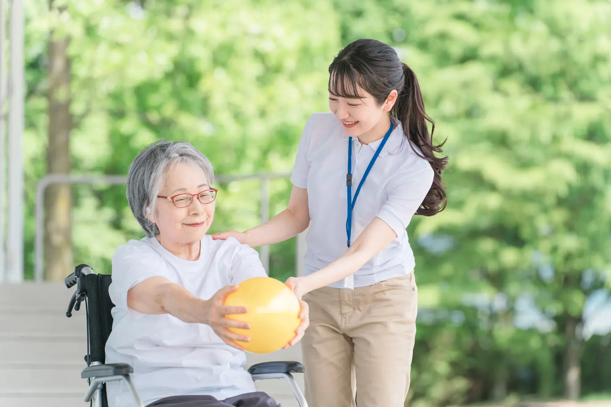 車いすのご高齢の女性と若い女性が黄色のボールを持っている