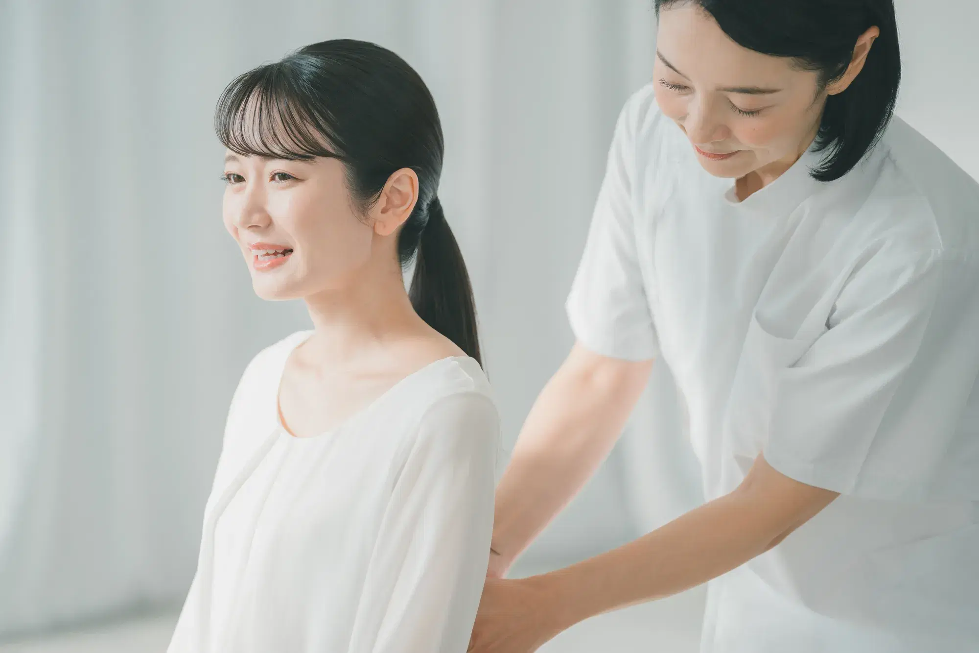 白い服を着た女性の背中を白衣を着た女性が押している