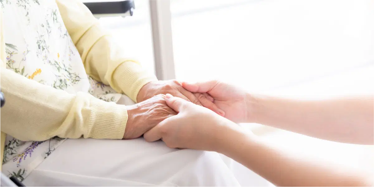 年配の女性の手を若い人が握っている