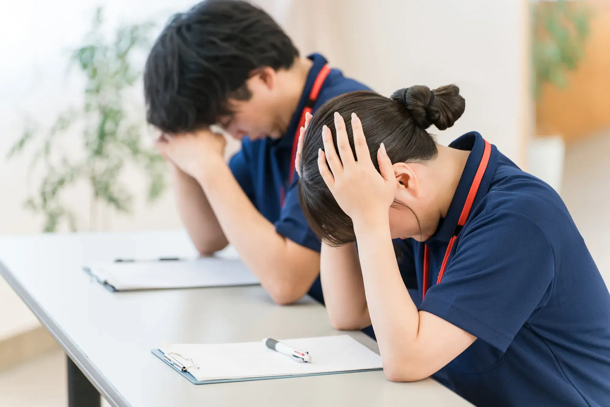 紺色の服を着た男女が頭に手を添えて困る