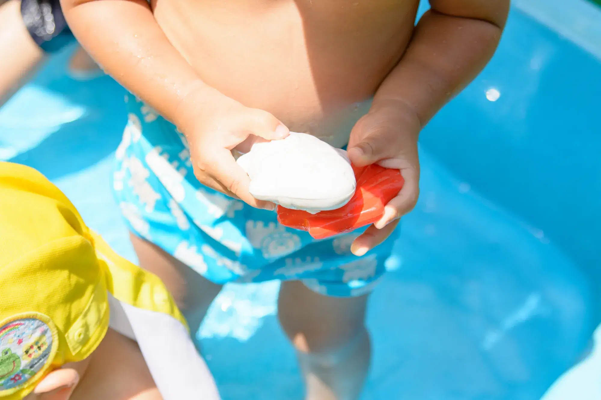 水色の水着を着てプールに入っている子供がおもちゃを持っている