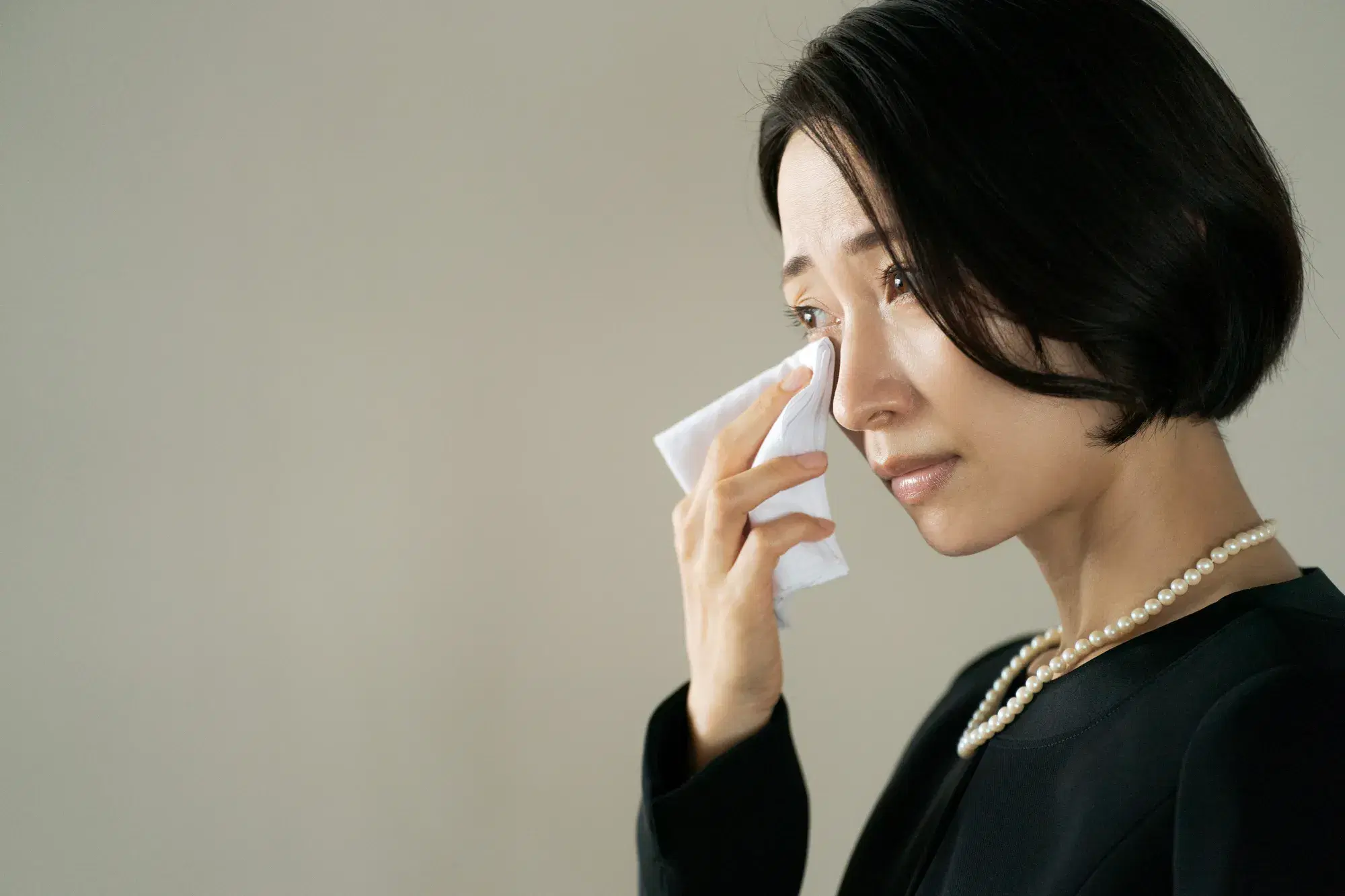 喪服を着た女性が涙をハンカチで拭っている。