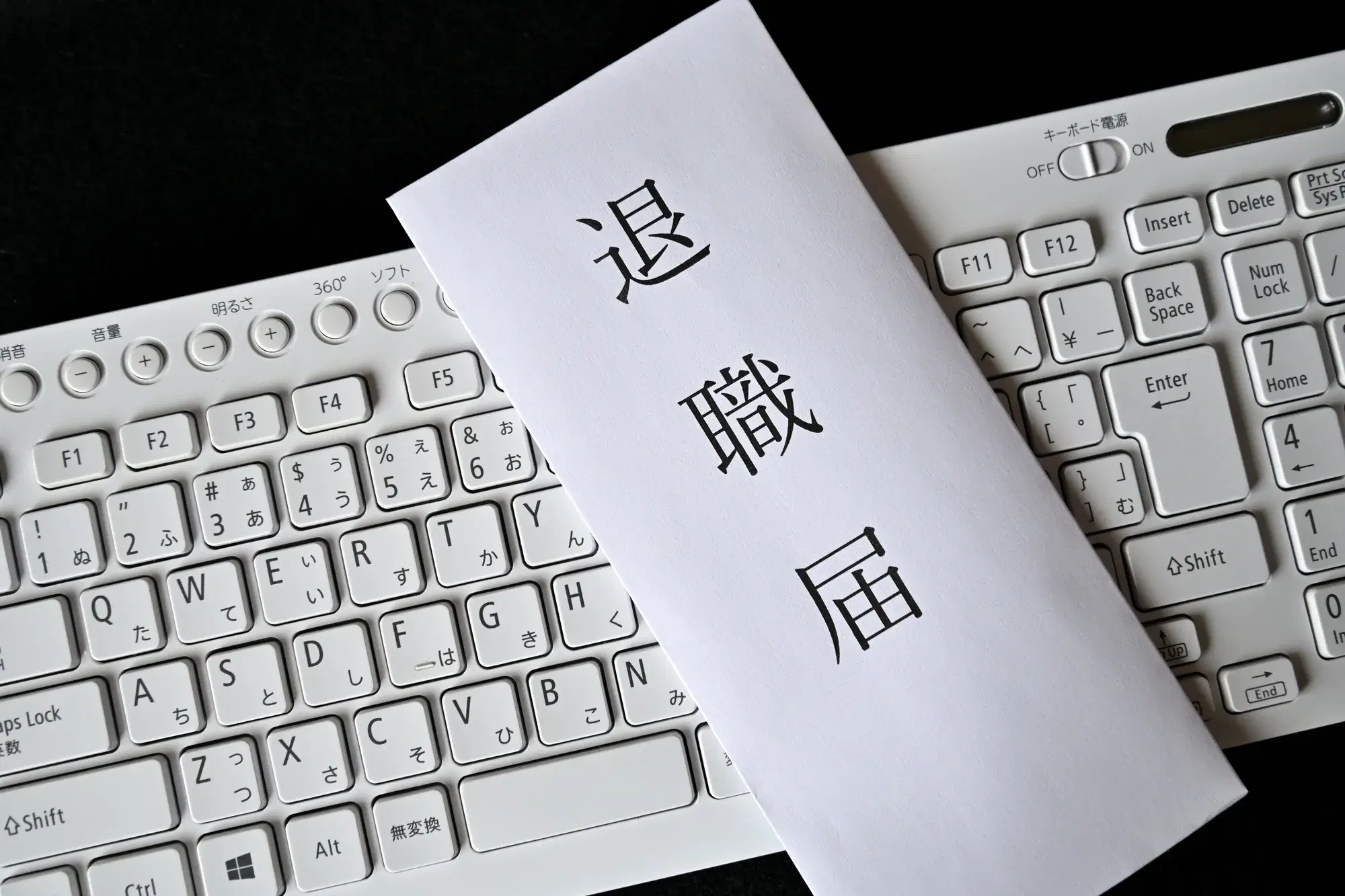 白色のパソコン用キーボードの上に「退職届」と書かれた封筒が置かれている様子が写っている。