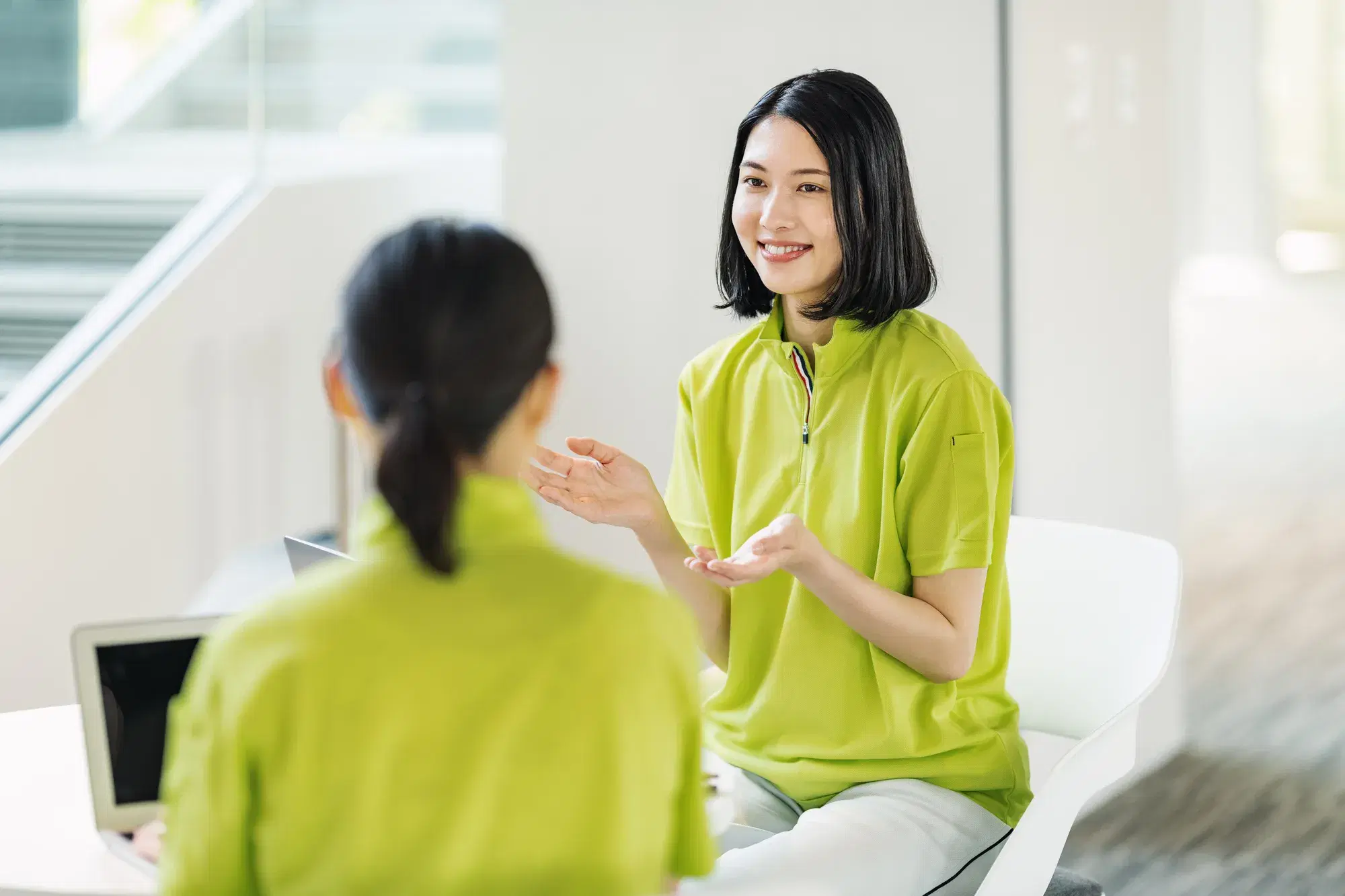 黄緑色の服を着た女性2人が会話