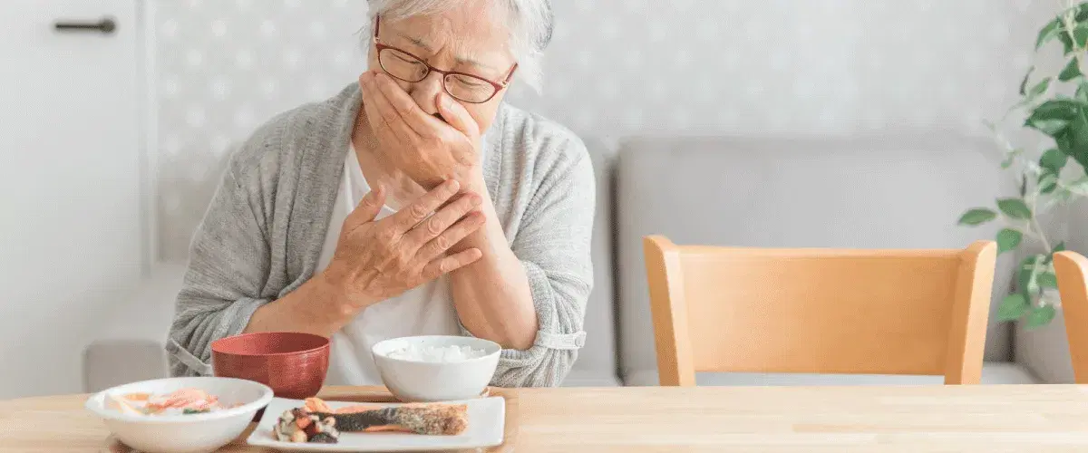 口元を抑える食事中の高齢男性