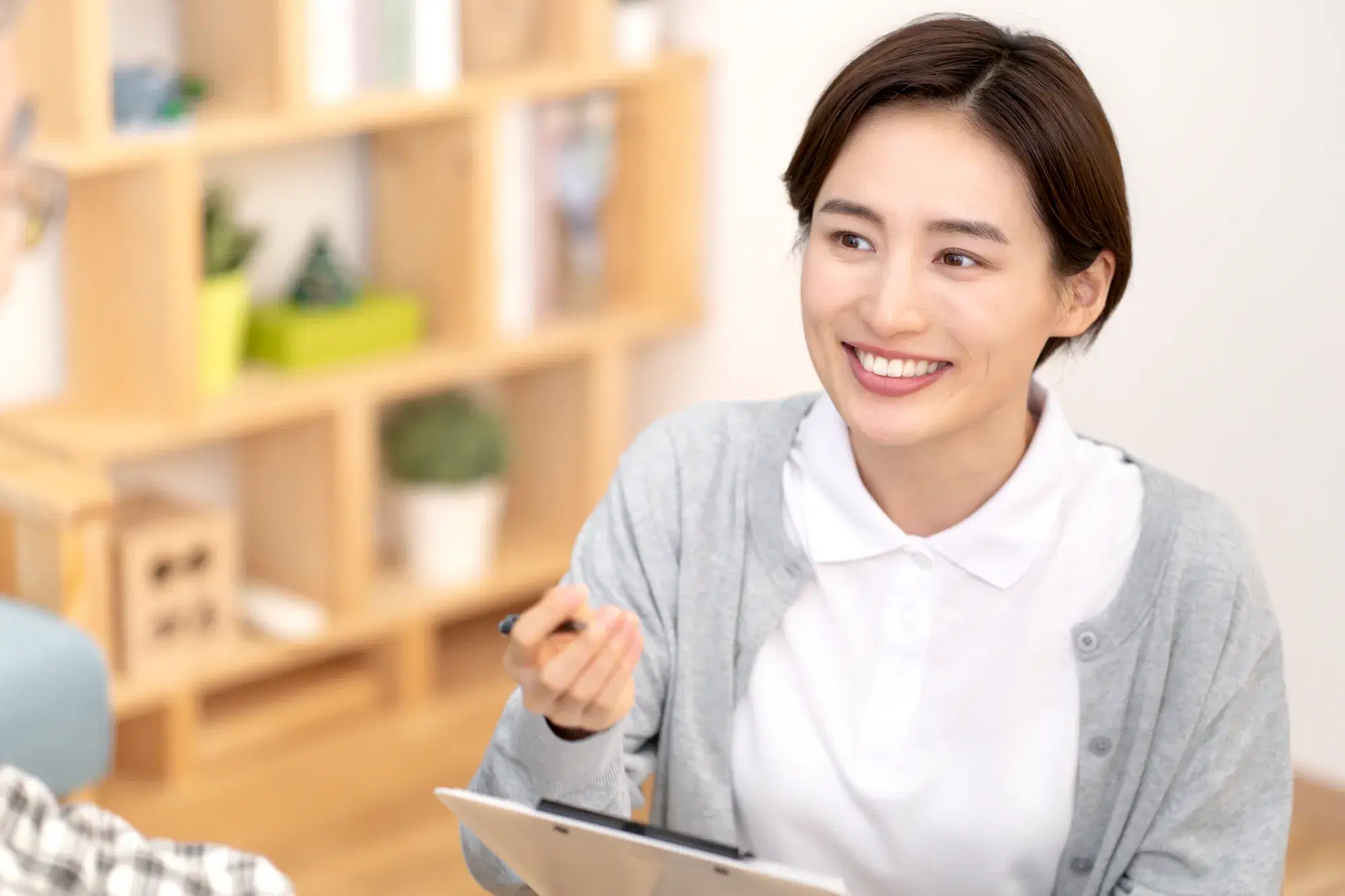 白衣の上に灰色のカーディガンを着た女性が話を聞いている