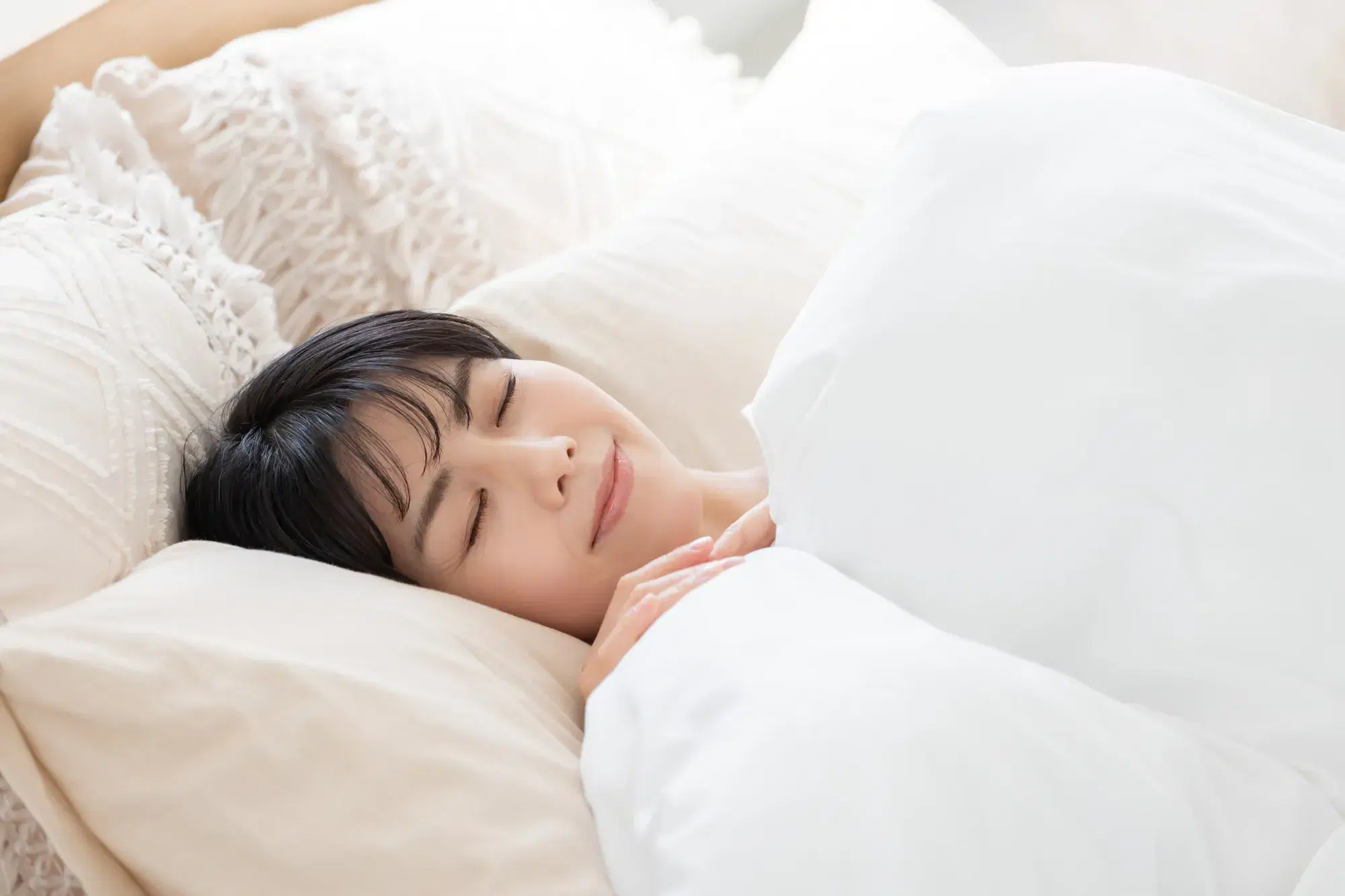 白い服を着た女性がベッドで布団をかけて寝ている。