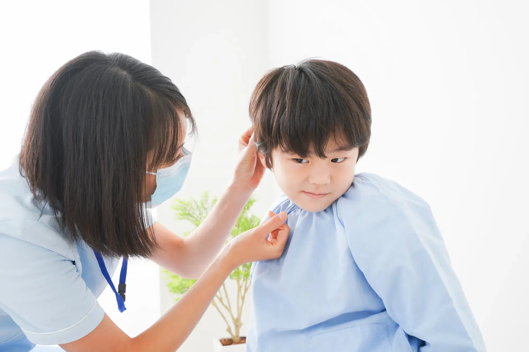 水色の服を着た子供が水色の服を着た看護師に耳を見せている