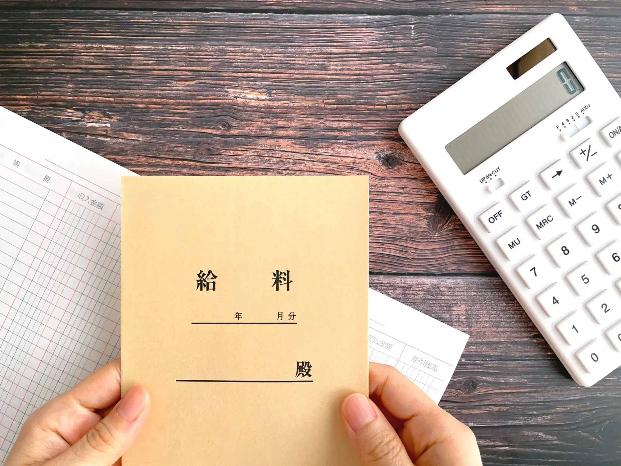 机の上に白い電卓と通帳と両手で給料袋を所持