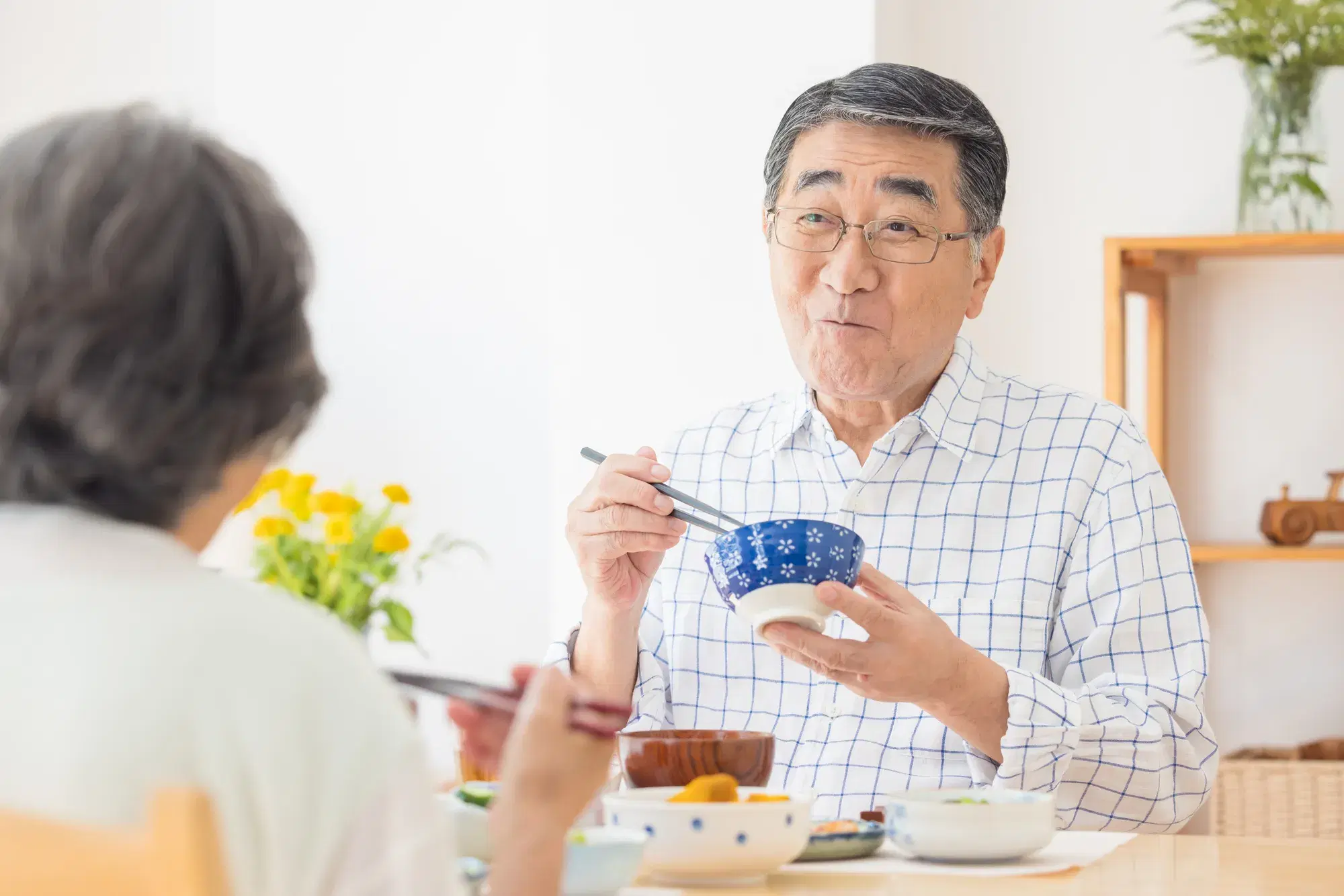 チェック柄の服を着た年配の男性と白い服を着た年配の女性が食事