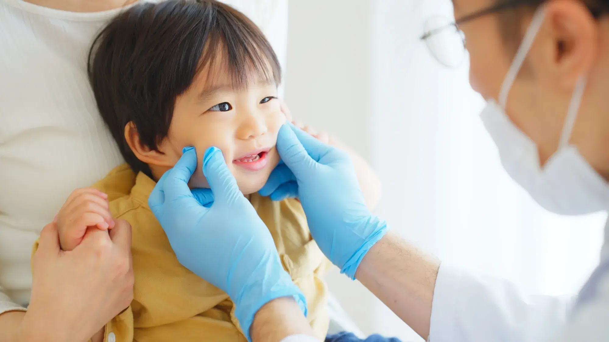 歯科医師が青いゴム手袋を着用した手で子どもの歯を診察