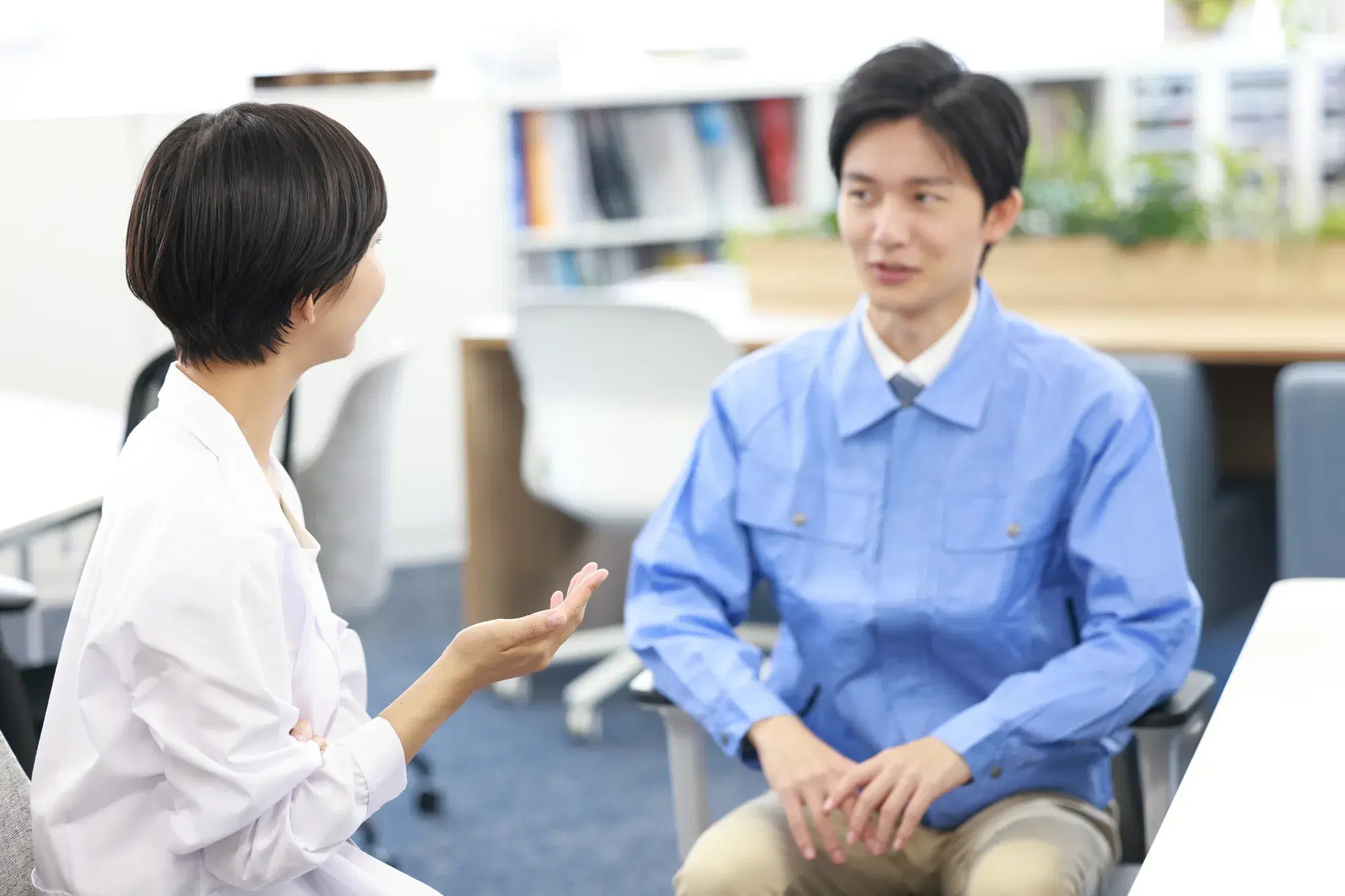 青い作業着を着た男性と白衣を着た女性が座りながら話している
