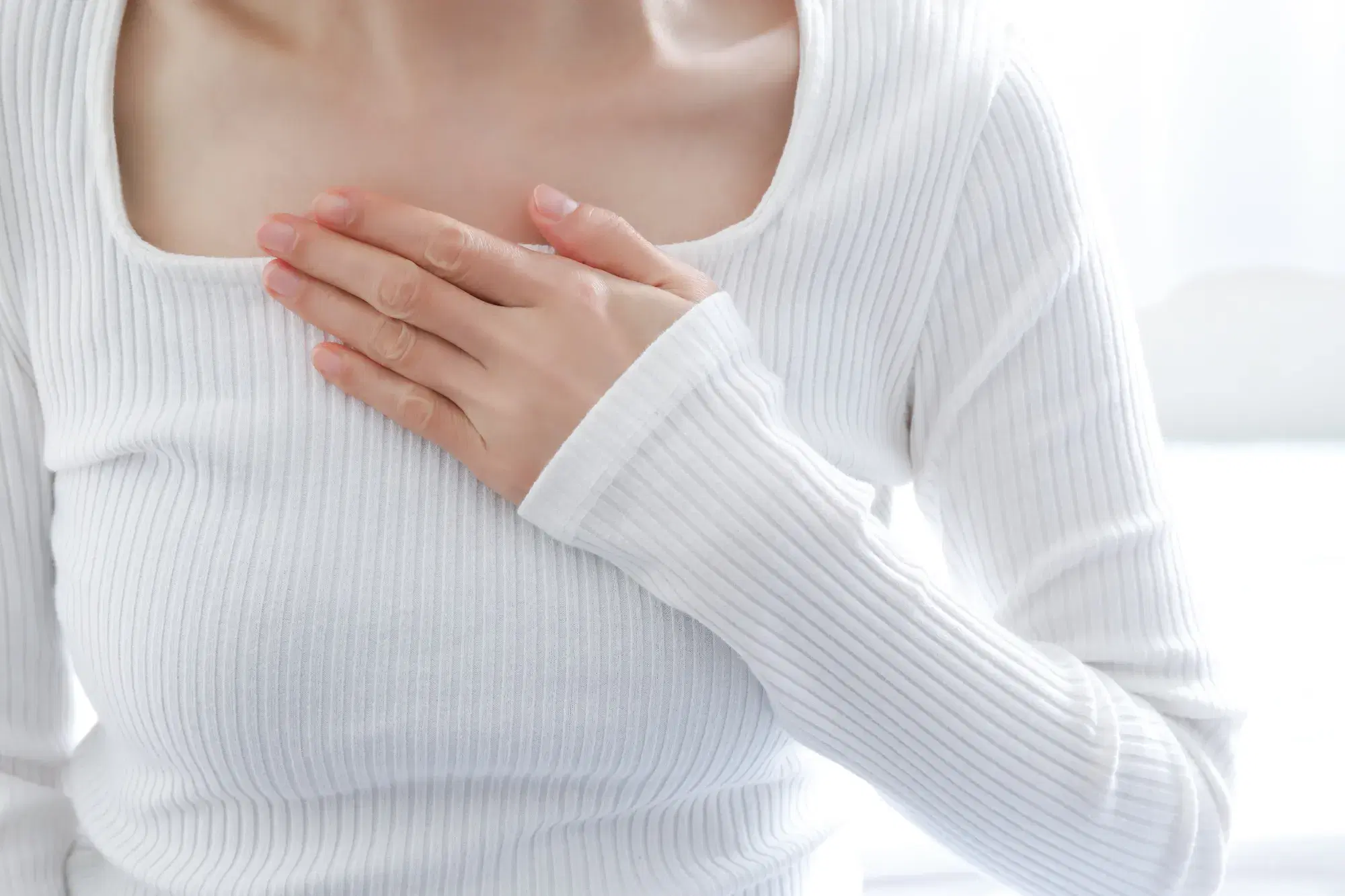 白い服を着た女性が鎖骨のあたりに手を当てている