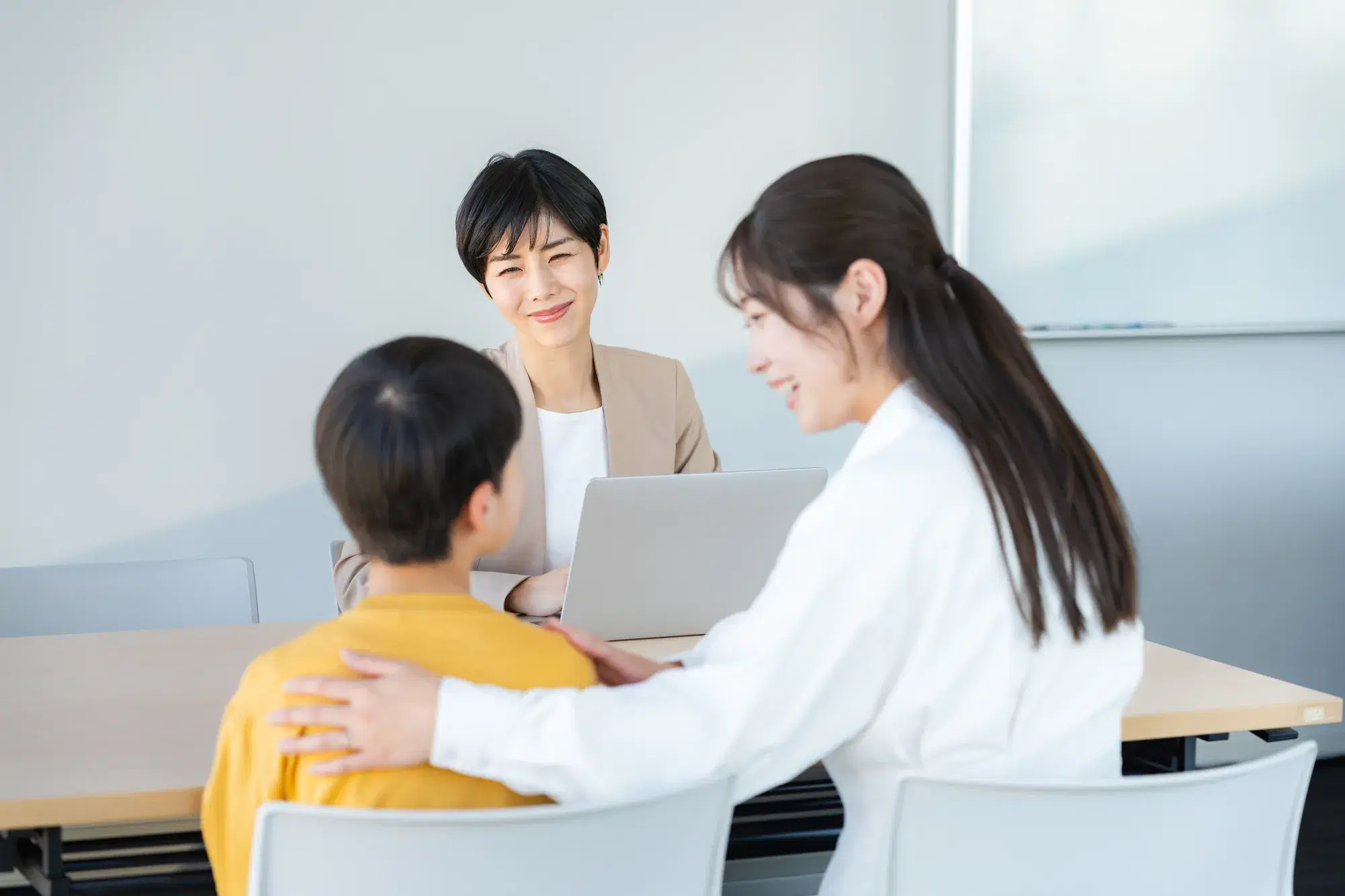 小学生くらいの子供と子どもの背中に手を回す母親と向かいに座るカウンセラーの女性