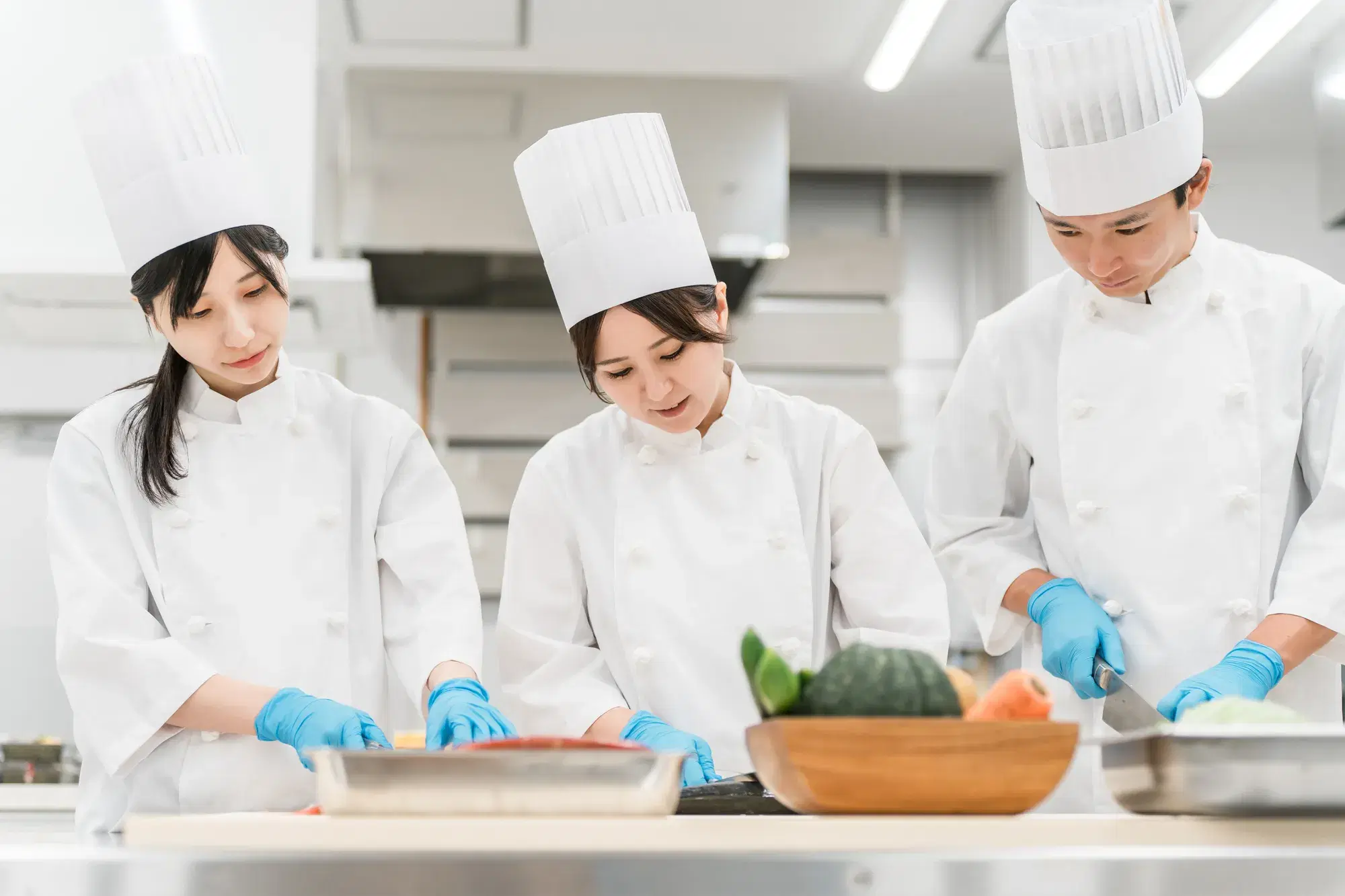白い作業服を着た複数の料理人が青い手袋をつけて作業している