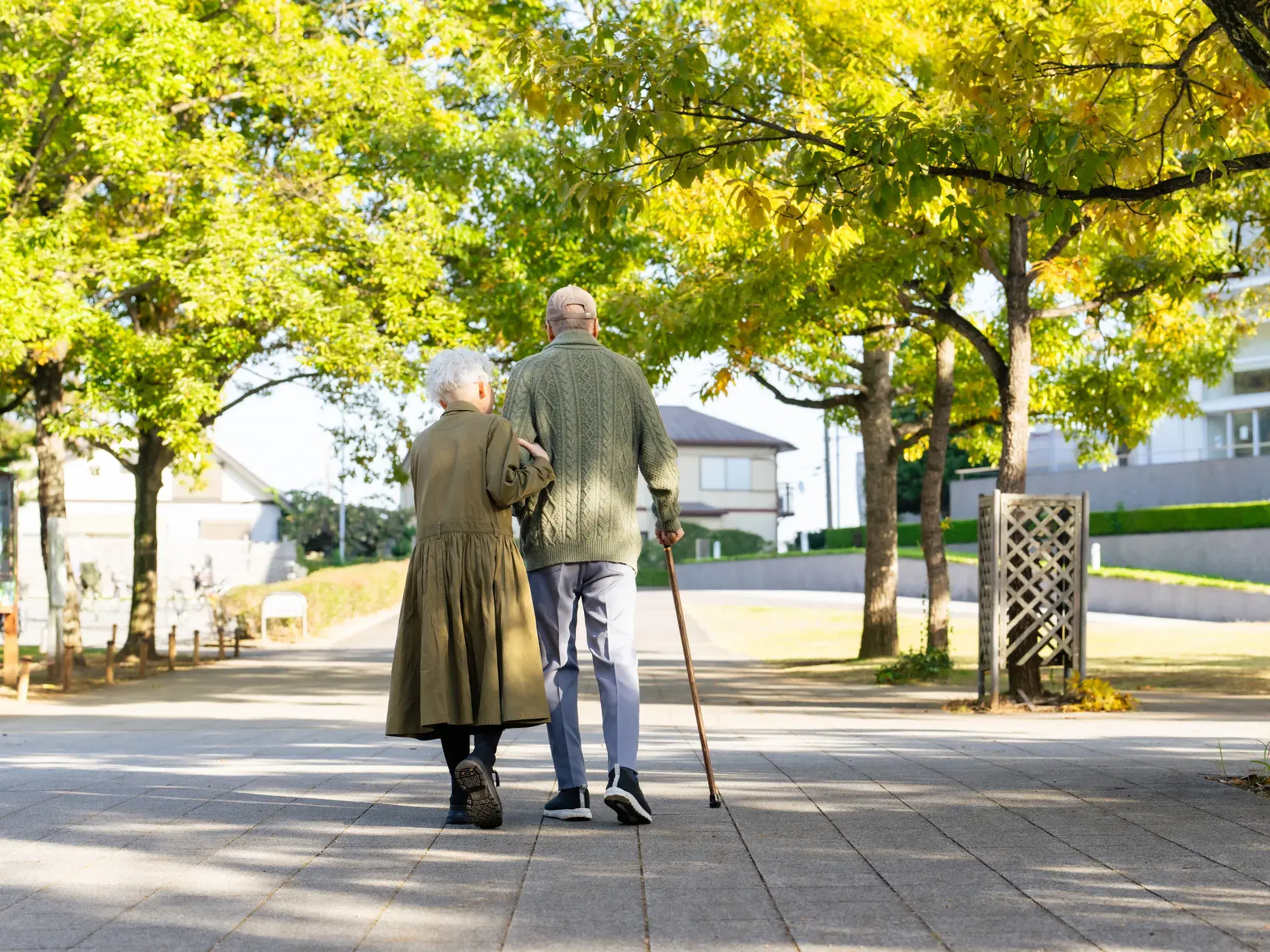 薄緑色の服を着た杖を突いて歩く年配の男性と腕を組んであるく薄緑色の服を着た年配の女性