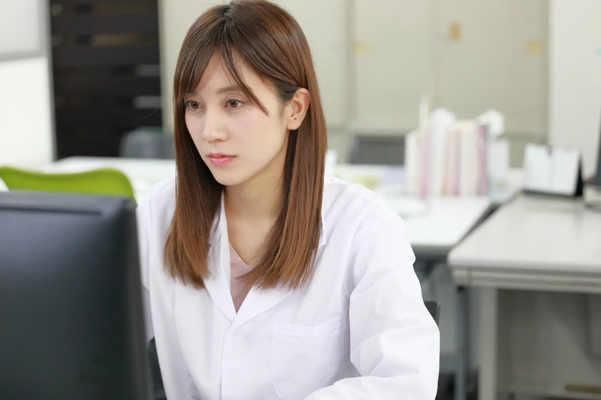 茶髪の白い服を着た女性がパソコンに向かって作業