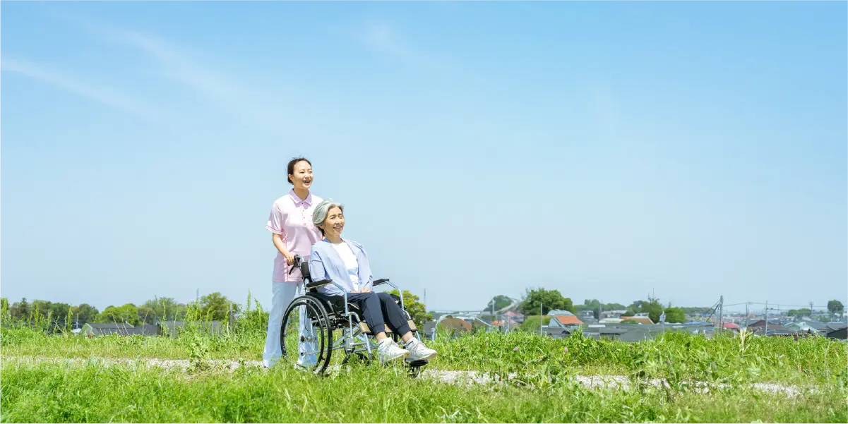 青空の下で車椅子に乗る年配の女性と職員の女性