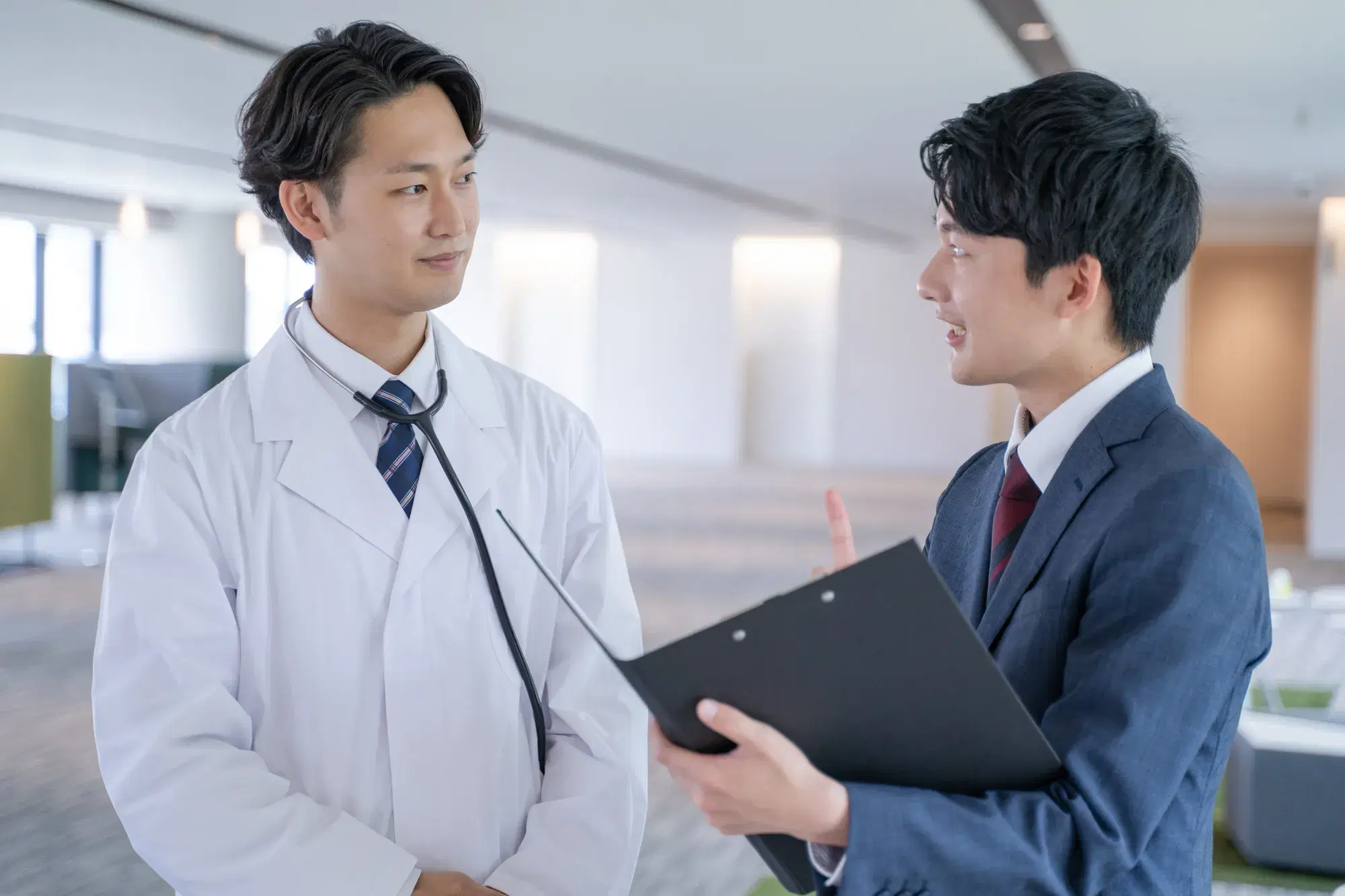 白衣を着た男性と黒いバインダーを持った紺色のスーツを着た男性