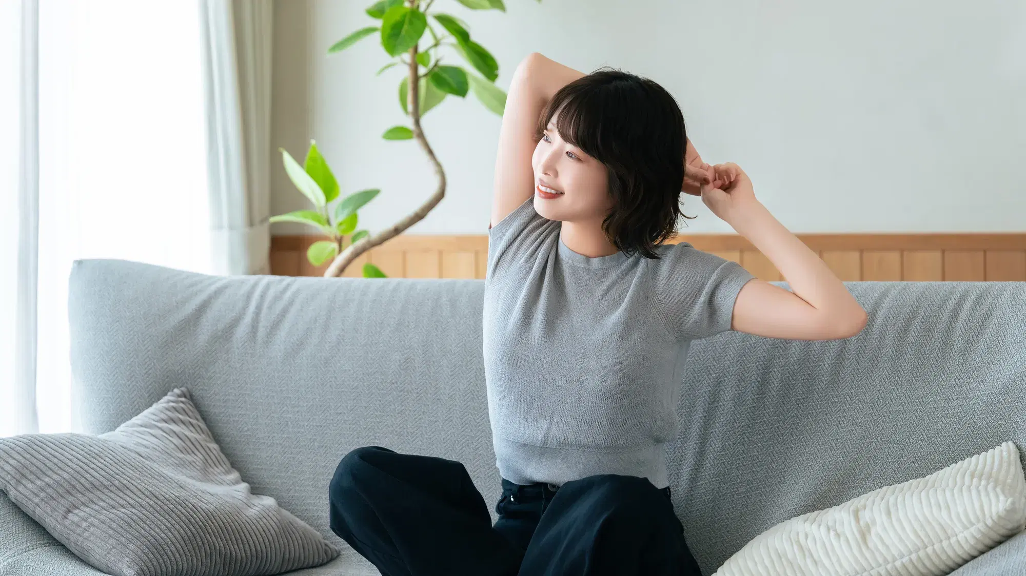 灰色のソファーの上でストレッチをする灰色の服を着た女性