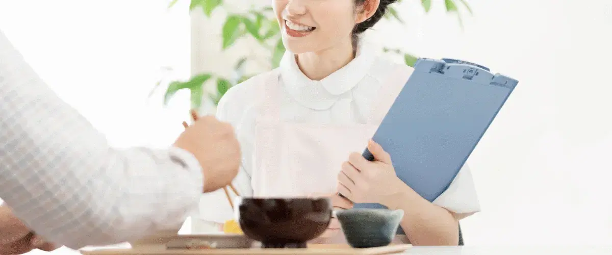 食事をしている高齢男性と笑顔で会話している介護職員女性