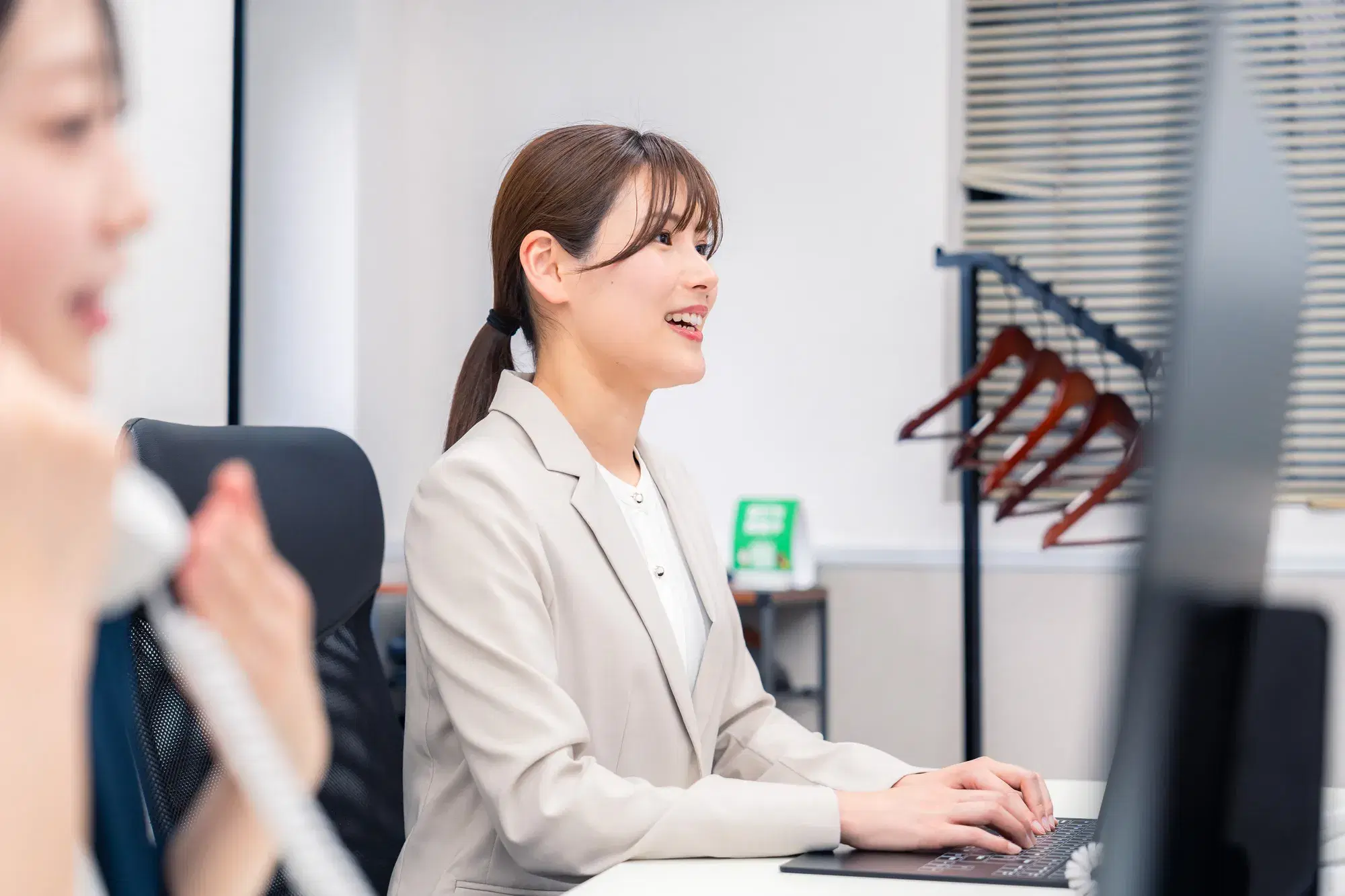 手前に電話対応している女性と奥側に灰色のスーツを着てパソコンを操作している女性