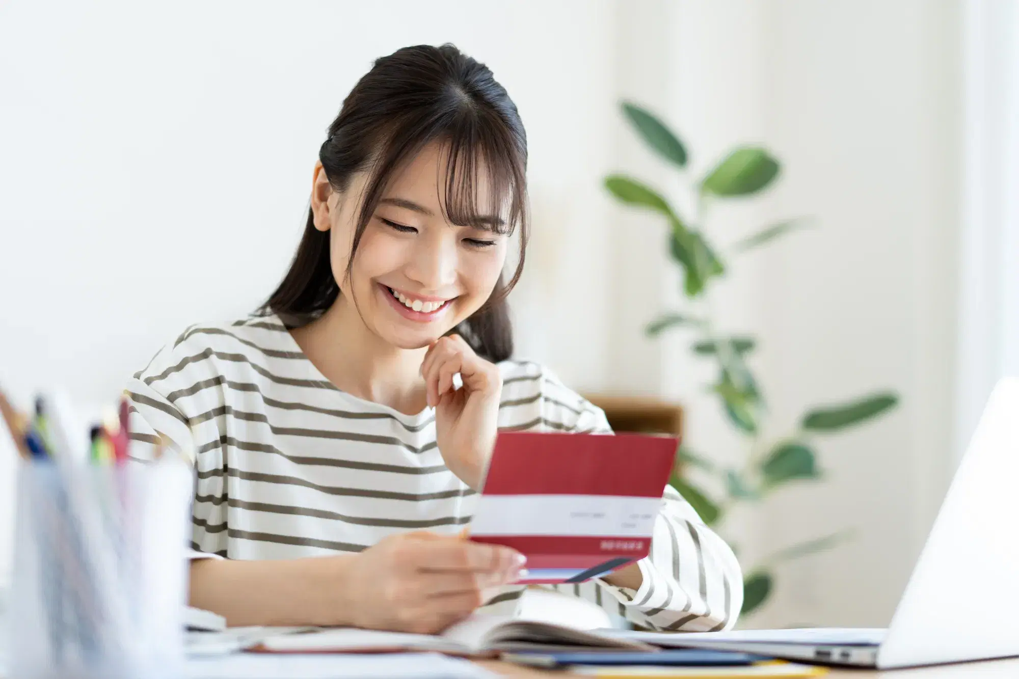 ボーダーの服を着た女性が赤い通帳を見て笑っている。