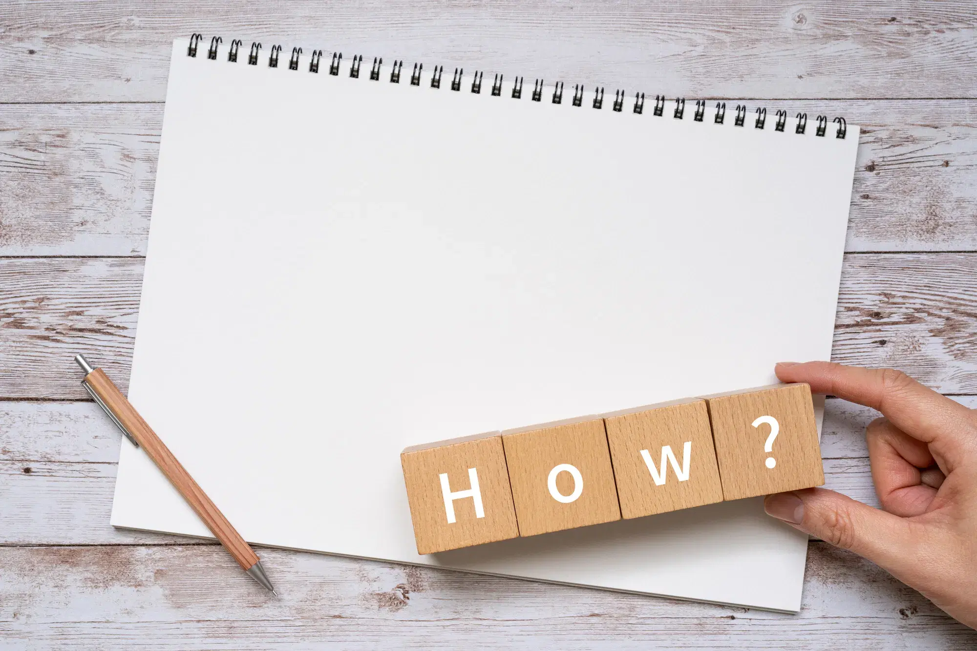ノートの上に鉛筆とHOW?と白い文字で書かれた積木が置かれている